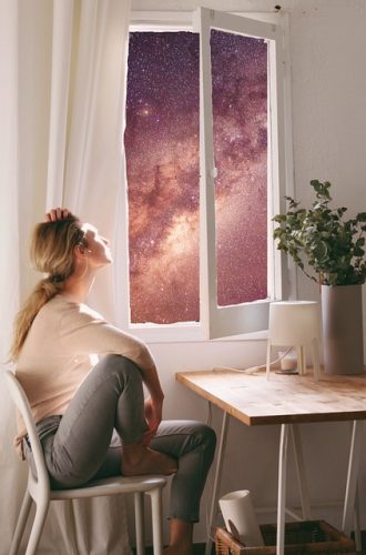 femme blonde pensive assise devant fenêtre ouverte regarde les étoiles